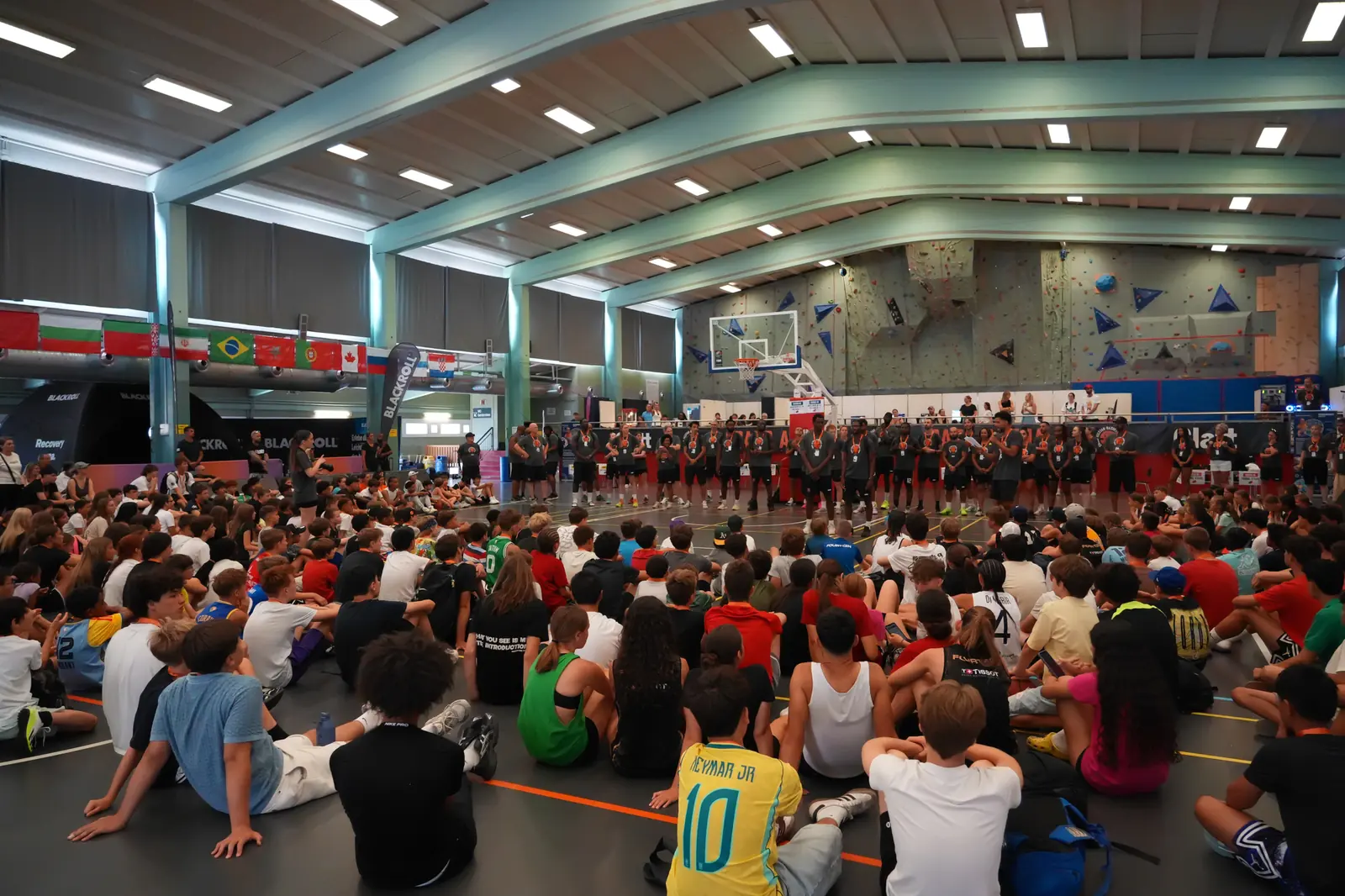 Eine grosse Gruppe Camp-Kinder sitzt bei der Eröffnung in der Sporthalle